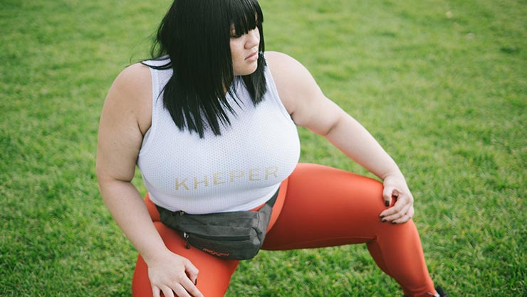 Woman in tank top, leggings, and fanny pack kneels in grassy field