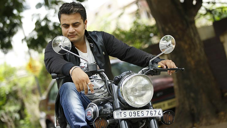 Man in blue jeans and black jacket sits on motorcycle