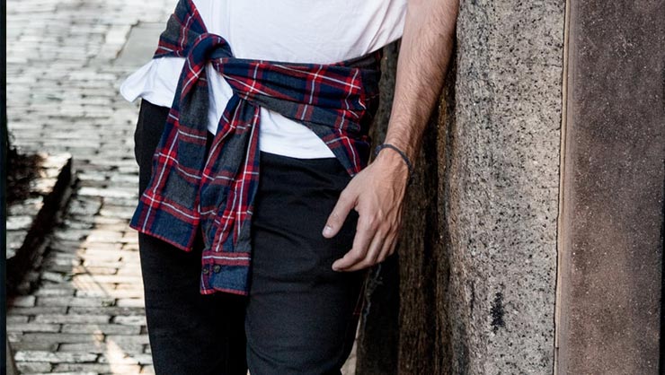 Man in white tee and plaid shirt leans on piller