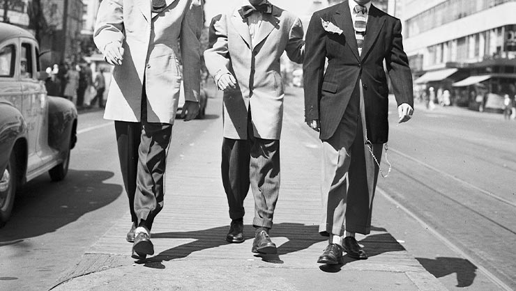 Three men in zoot suits walk down a street.